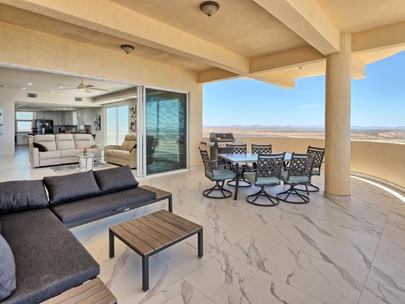 Patio with a dining table and grill, opened to a bright living room and a desert landscape beyond.