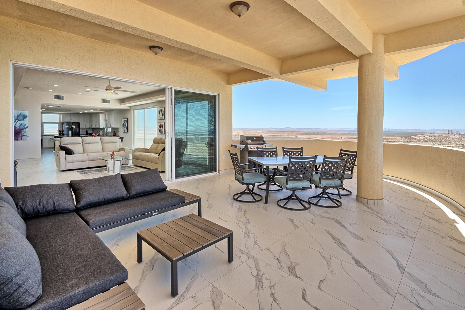 Patio with a dining table and grill, opened to a bright living room and a desert landscape beyond.