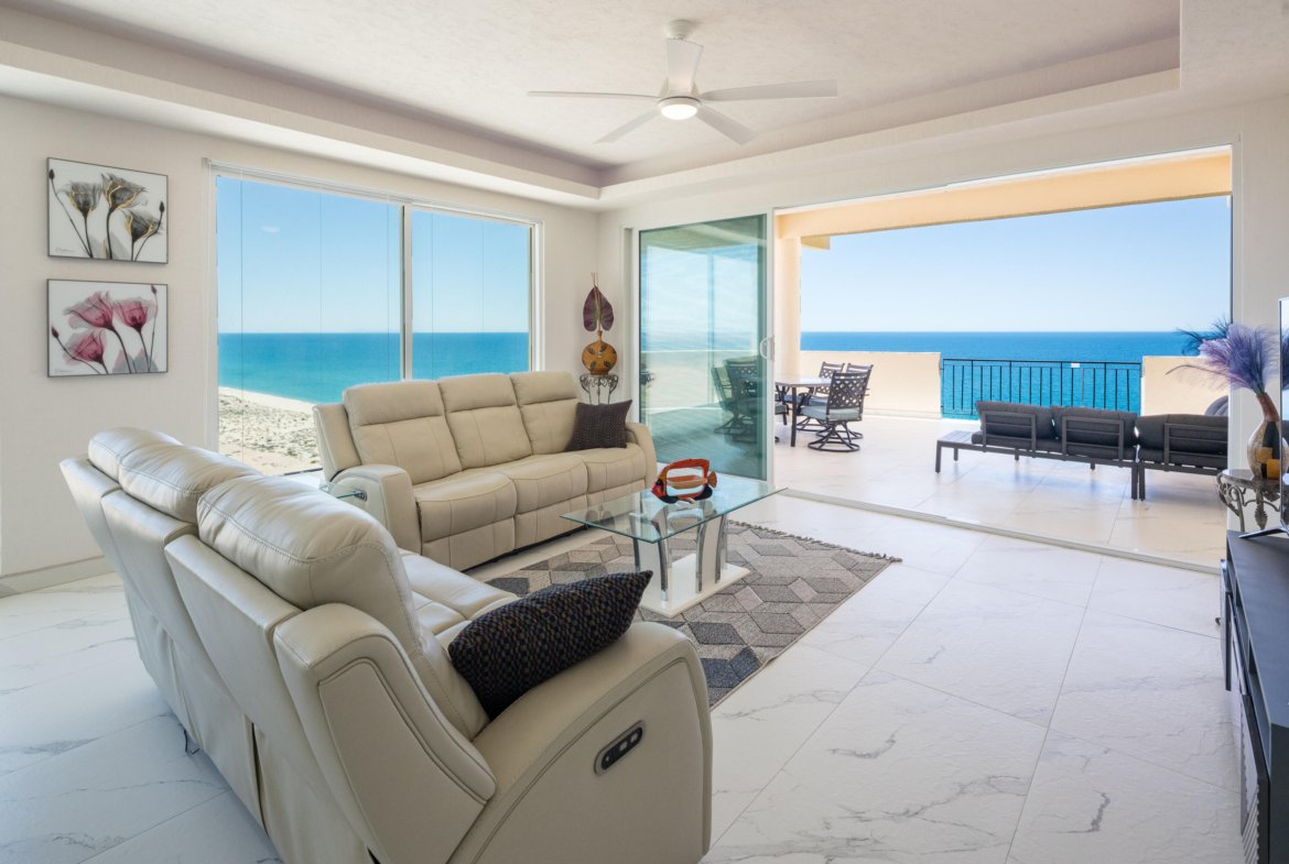 Bright living room with beige leather sofas facing large windows and a ocean-view balcony beyond the sliding doors