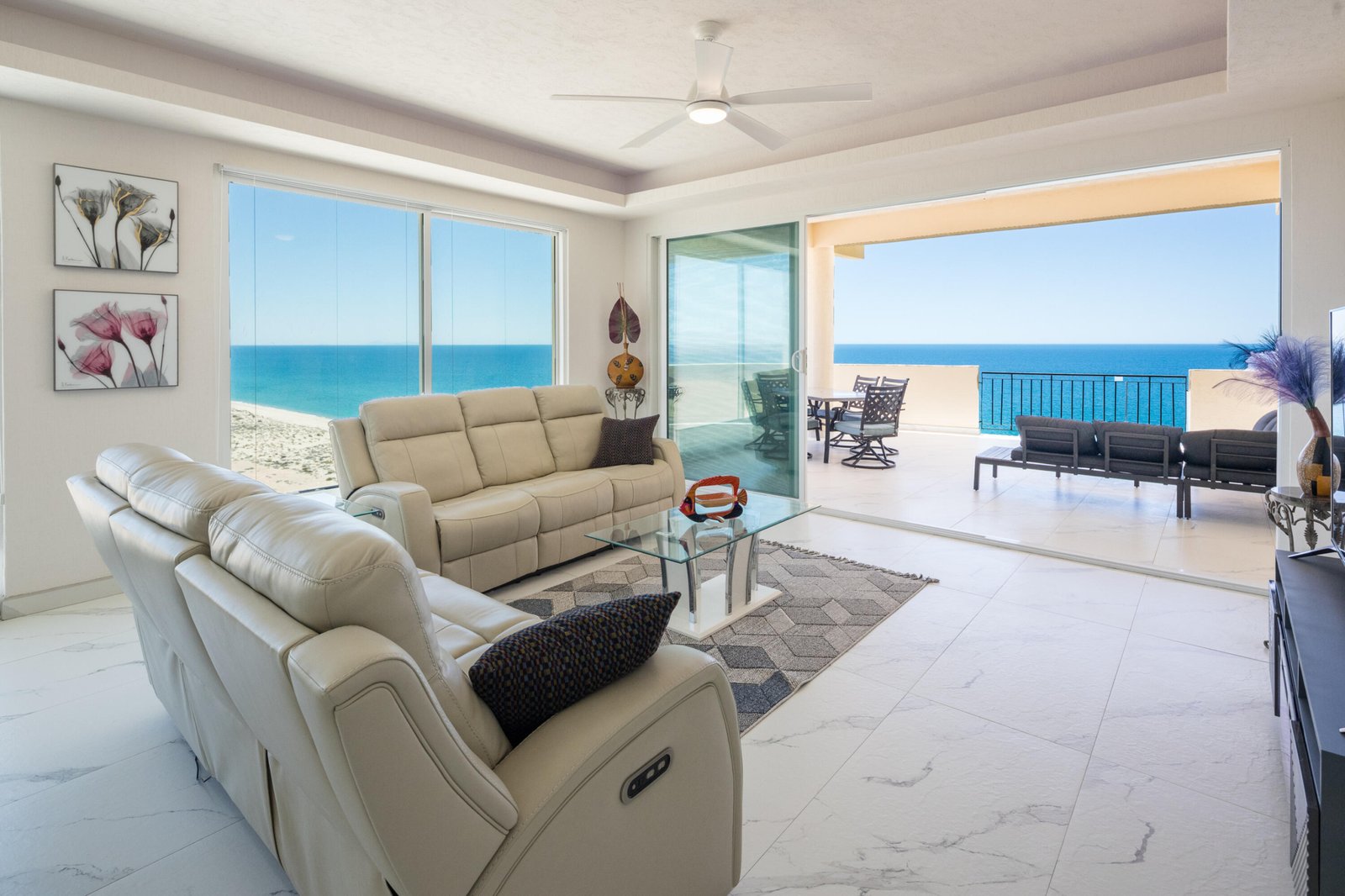Bright living room with beige leather sofas facing large windows and a ocean-view balcony beyond the sliding doors