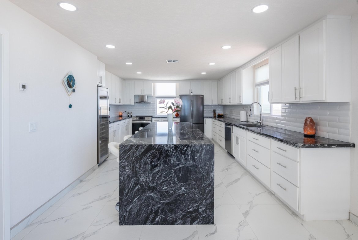 Bright white kitchen with a black marble island center, white cabinets, and stainless appliances.